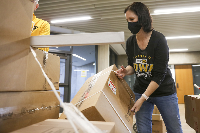 A woman wearing a mask pulls a box from a pallet. 
