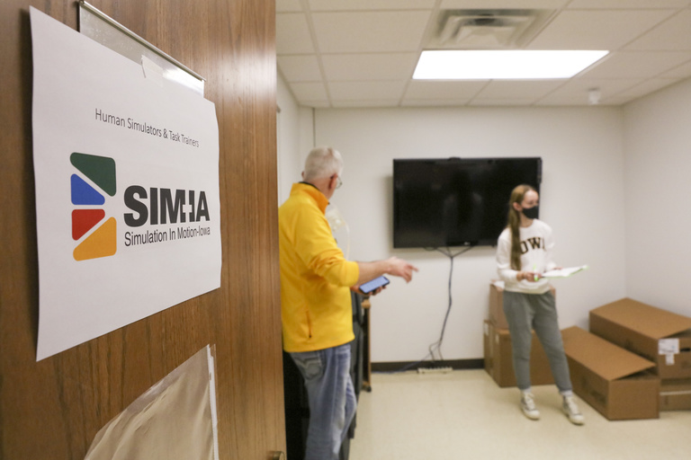 two people and boxes are seen through open door. Door sign says Sim-IA