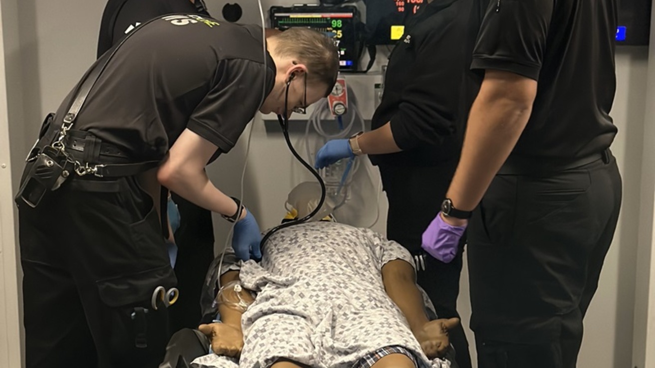 Four healthcare professionals around a table on a manikin on it